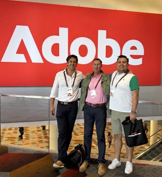 With colleagues in front of the Adobe wall at Summit, Learning Manager swag in hand